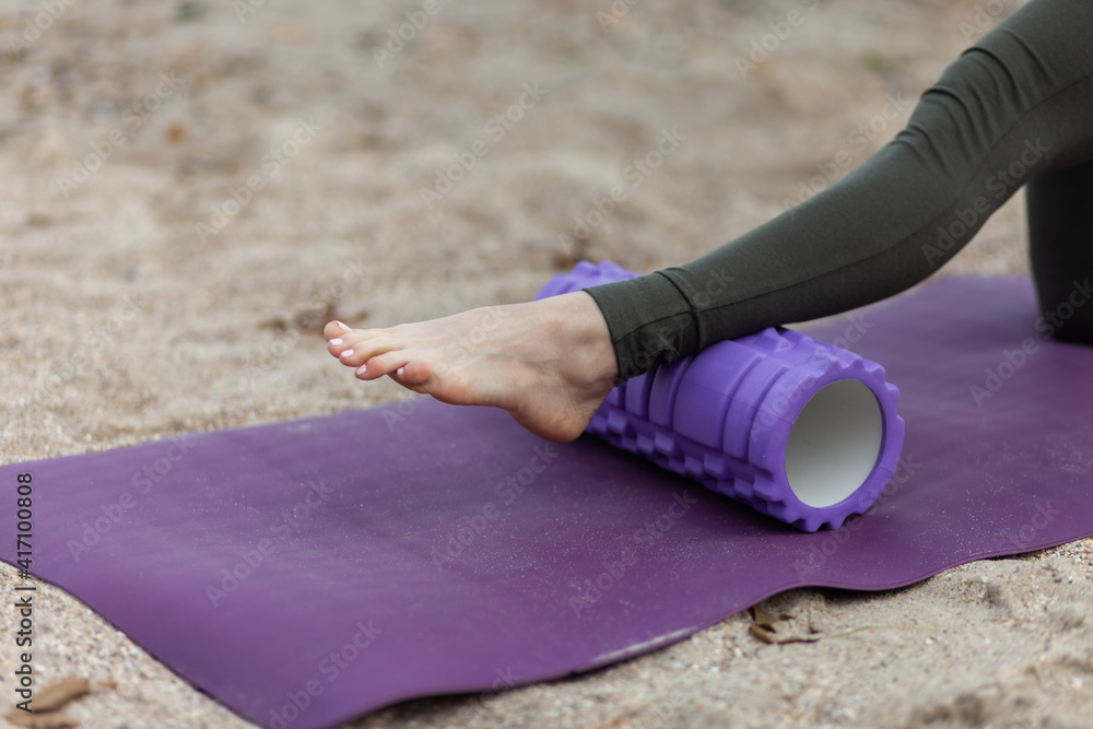 Active fit woman relax muscles with massage roller on mat at beach. Active fit woman relax muscles with massage roller on mat at beach.