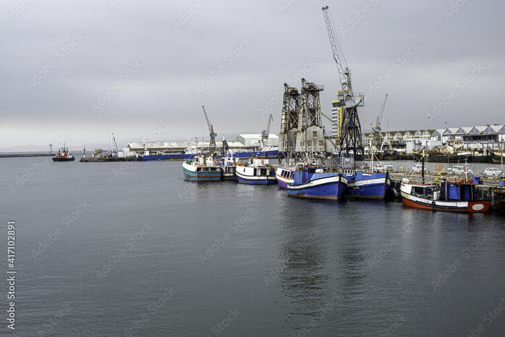Fototapeta premium Hafen mit Fischerbooten und Gebäuden mit Arbeitskran bei bedecktem Himmel