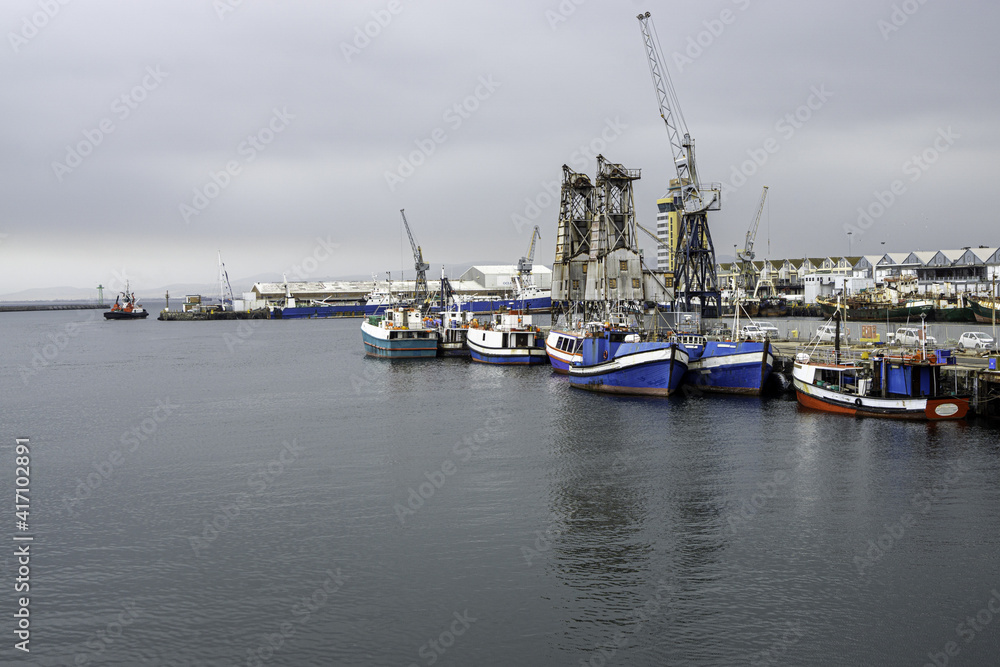 Hafen mit Fischerbooten und Gebäuden mit Arbeitskran bei bedecktem Himmel