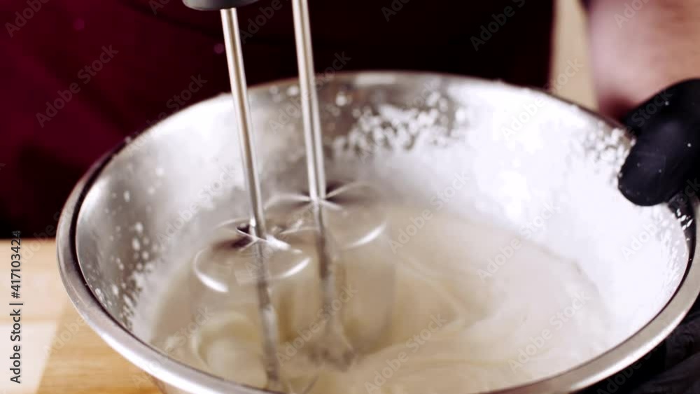 Male chefs hands whipping the egg protein in the metal using the mixer and adding ingredients like sugar, starch, salt, species Male chefs hands whipping the egg protein in the metal using the mixer and adding ingredients like sugar, starch, salt, species