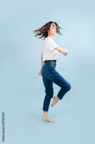 Dynamic contemporary dancer poses in front of blue studio background. She's bending knee with straightened ankle, like horse. In a body rotating motion.