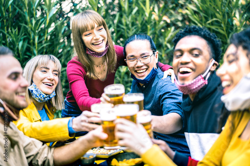 Young people toasting beer with opened face masks - New normal life style concept with happy friends having fun together drinking at brewery bar garden - Bright contrast filter with focus on asian guy © Mirko Vitali