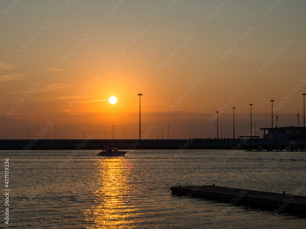 The boat crosses the path of glare into the sea under the setting sun in the sky