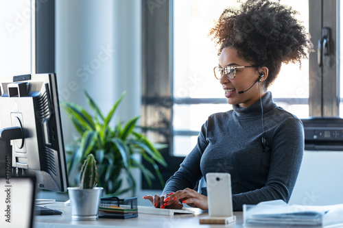 Canvas Print Beautiful young afro business woman working while making video call with computer sitting in the office