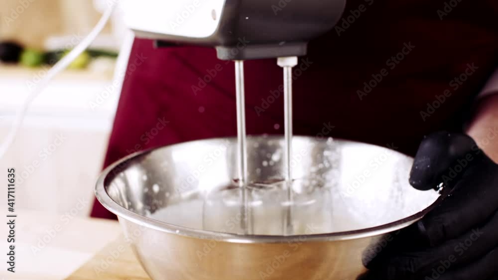 Male chefs hands whipping the egg protein in the metal using the mixer and adding ingredients like sugar, starch, salt, species Male chefs hands whipping the egg protein in the metal using the mixer and adding ingredients like sugar, starch, salt, species
