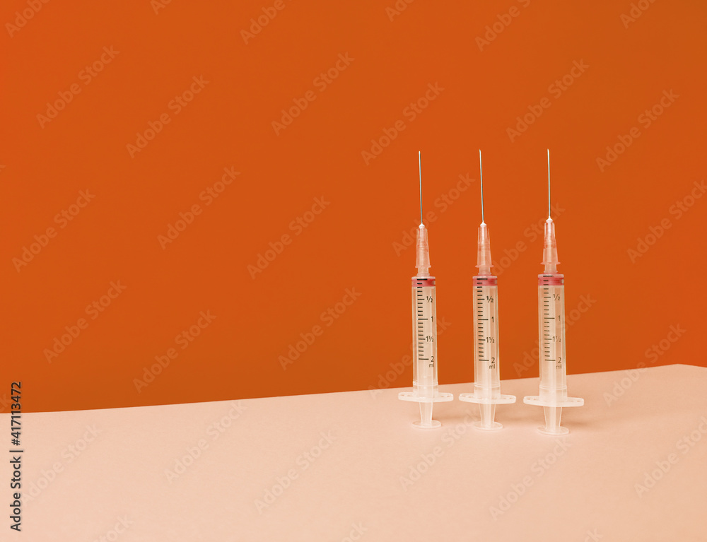 Three syringes on orange background with trendy skyline and copy space. Three syringes on orange background with trendy skyline and copy space.