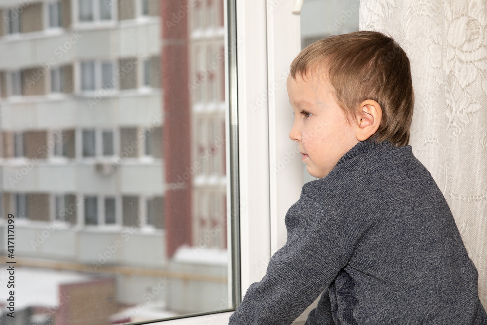 A 6-year--old boy is bored and looks out the window from his apartment A 6-year--old boy is bored and looks out the window from his apartment