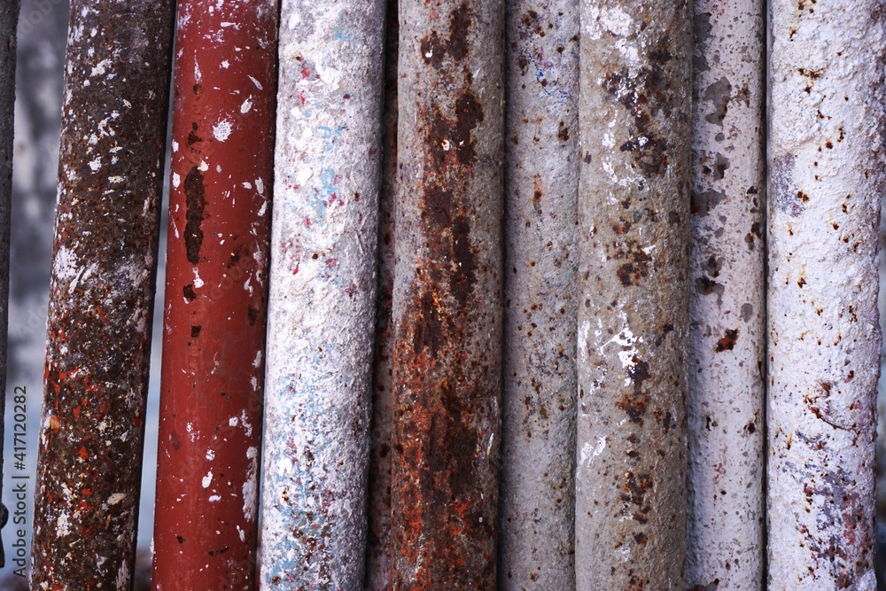 Industrial background pattern with funky paint spattered rusted metal scaffold pipes lined up in a horizontal row Industrial background pattern with funky paint spattered rusted metal scaffold pipes lined up in a horizontal row