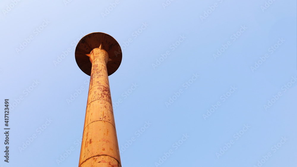 Old metal tower of water tank. Orange water reserve of the community water supply system and the morning sun in view below. On a bright blue sky background with copy space. Selective focus