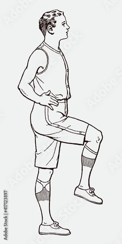Young man from early 20th century in sportswear raising one leg and holding balance, in side view