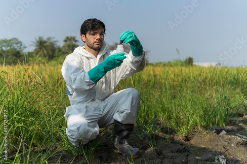 A technician in overall protective suit collecting samples of soil potentially contaminated by toxic material ,soil quality monitoring concept ,ph checking on field.