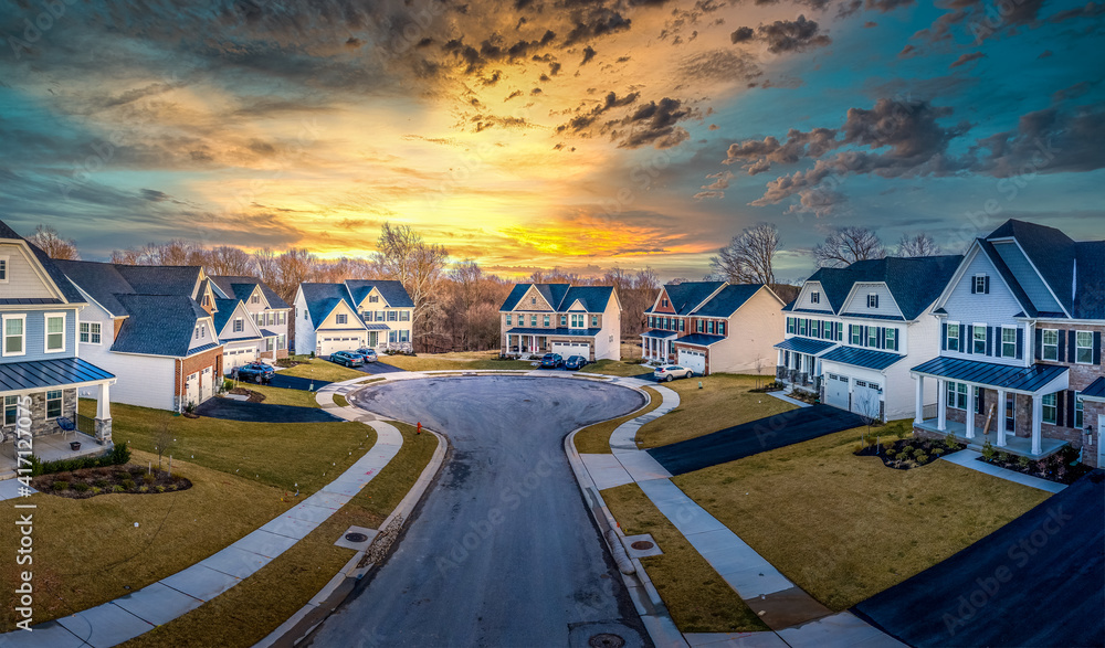 Typical American dead end street surrounded by luxury two story single family homes in new residential East Coast USA real estate suburban neighborhood dramatic colorful yellow orange sunset sky