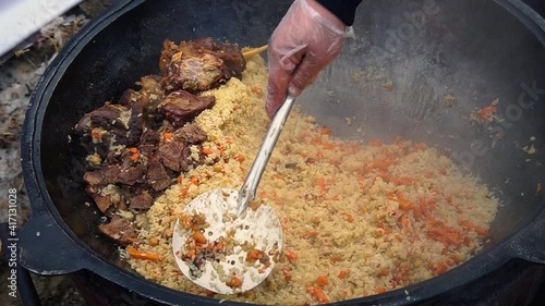 Prepare pilaf in a large frying pan. A dish of rice and pieces of vegetables. Steam comes from a hot lunch. Home kitchen. Pilaf is stirred with a wooden spatula.