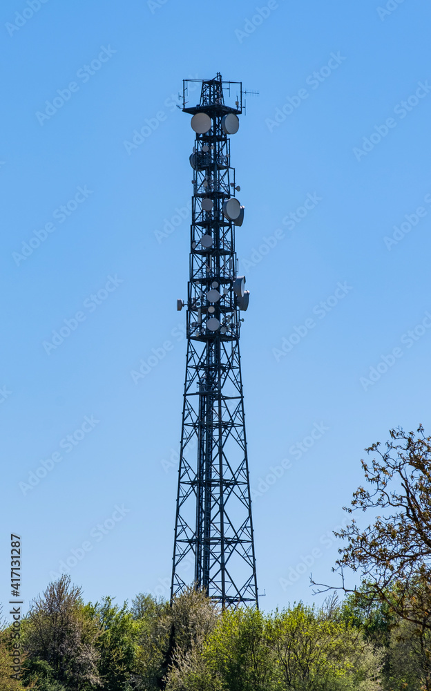 telecommunication mast, TV antennas wireless technology against blue cloudless sky over green hedges