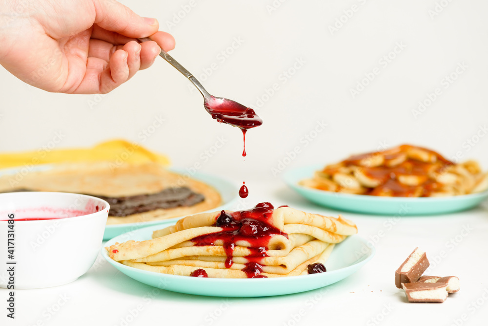 blini pancakes with red berry jam closeup on a blue plate on a light