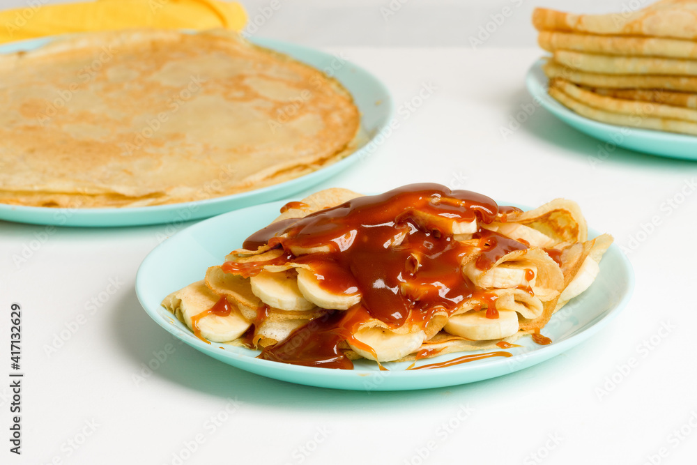 blini pancakes with caramel, dripping on a spoon levitation close-up on a blue plate on a light background . traditional Russian holiday is a symbol of spring and sweet dessert blini pancakes with caramel, dripping on a spoon levitation close-up on a blue plate on a light background . traditional Russian holiday is a symbol of spring and sweet dessert