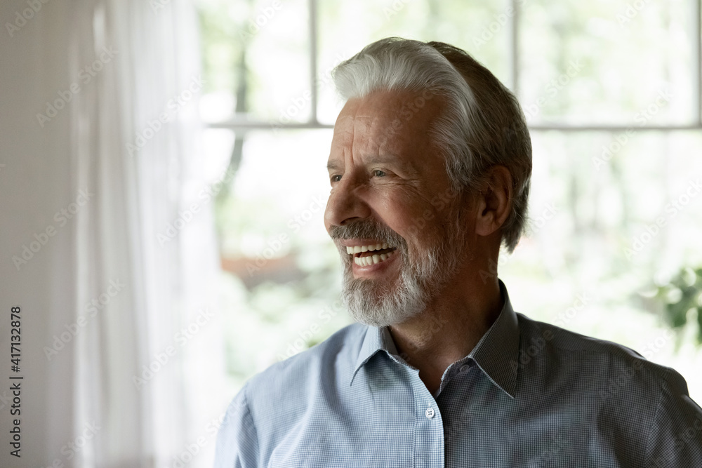 Naklejka premium Happy senior 70s aged man looking away and laughing at funny joke. Healthy mature older person having fun at home, enjoying retirement, having great health, getting good news. Elderly OAP age concept
