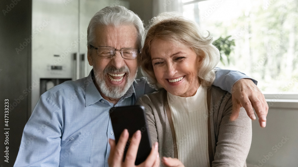 Happy retired family couple using mobile phone for video call together, talking to relations, getting good news, having fun, smiling and laughing. Carefree mature pensioners chatting online on cell Happy retired family couple using mobile phone for video call together, talking to relations, getting good news, having fun, smiling and laughing. Carefree mature pensioners chatting online on cell
