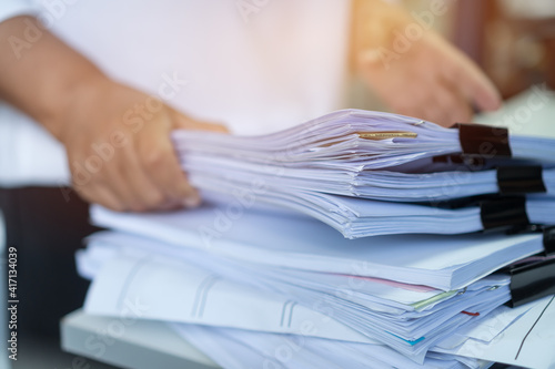 Employee checking business unfinished documents with stacks paper files and managing document achieves preparing meeting planing at busy work in financial office. Tax time in filing information photo