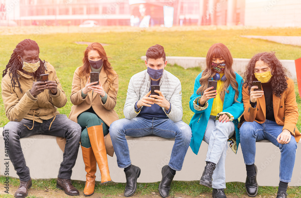 Obraz premium Group of trendy friends wearing face safety masks while watching videos on smartphone - Concept of new normal , technology and covid-19