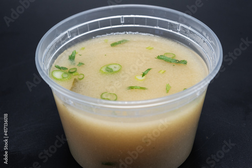Bowl of Miso soup shows delicious cloudy broth containing green onion, seaweed, and spicy flavor in clear container.