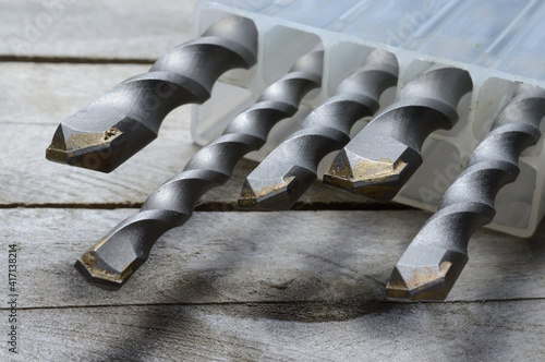 drills with carbide tipped hammer drill bits lie in a plastic case on a plank wooden background. close-up.