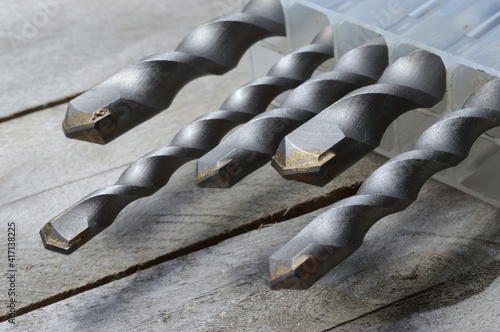 Photos drills with carbide tipped hammer drill bits lie in a plastic case on a plank wooden background
