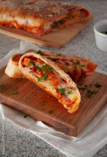 Closed pizza with ham, cheese and tomatoes on a wooden board