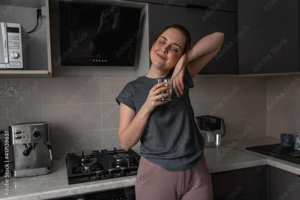 A young brunette woman stands in the kitchen and drinks water from a glass glass A young brunette woman stands in the kitchen and drinks water from a glass glass
