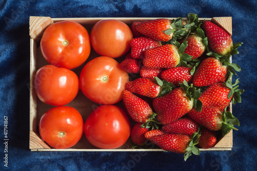 Food basket with strawberries and tomatoes on blue background. Vegetarian food and healthy ingredients.
