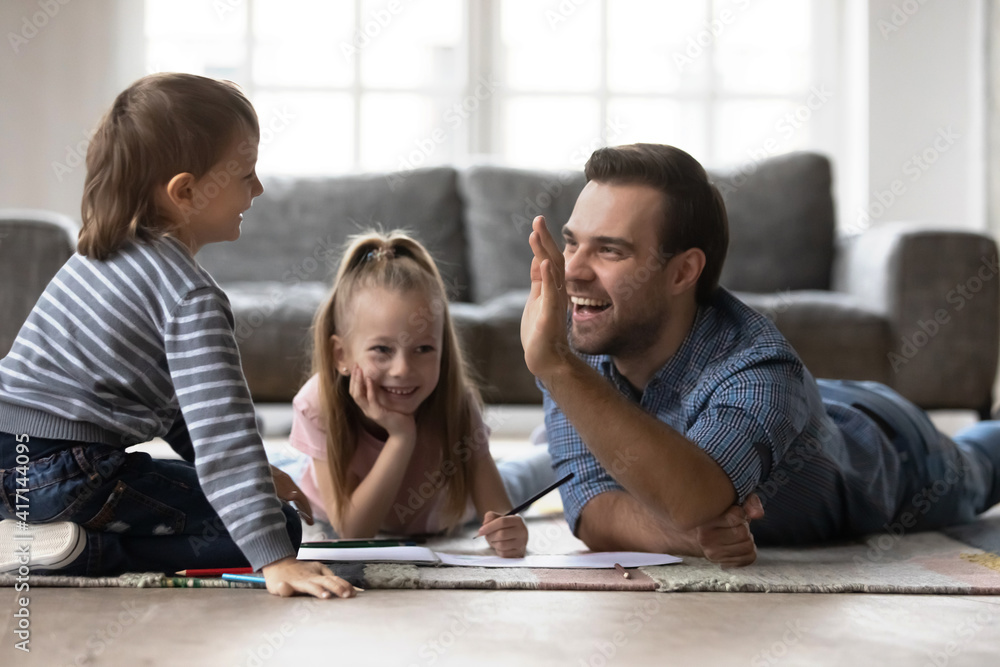 Best dad gives high five to happy little kid, plays and draws on heating floor. Father enjoys creative activity with preschooler children staying at home during coronavirus quarantine. Family time Best dad gives high five to happy little kid, plays and draws on heating floor. Father enjoys creative activity with preschooler children staying at home during coronavirus quarantine. Family time