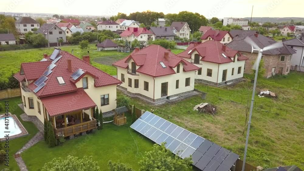 Aerial view of suburban homes and private house with green grass covered yard, solar panels on roof, swimming pool with blue water and wind turbine generator. Aerial view of suburban homes and private house with green grass covered yard, solar panels on roof, swimming pool with blue water and wind turbine generator.
