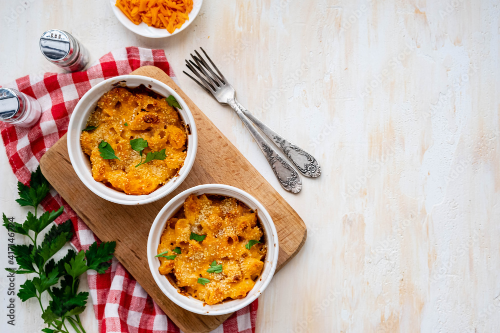 Two servings of mac and cheese, macaroni in cheese sauce, in white ceramic frames on a light concrete background. American cuisine. Two servings of mac and cheese, macaroni in cheese sauce, in white ceramic frames on a light concrete background. American cuisine.