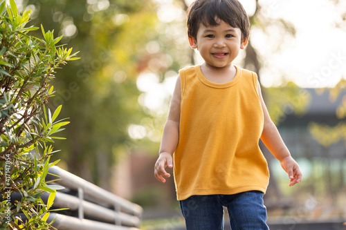 Child walking on the grass. Asian Little boy wear a yellow shirt walking around. Children playing in the playground with sunlight.
