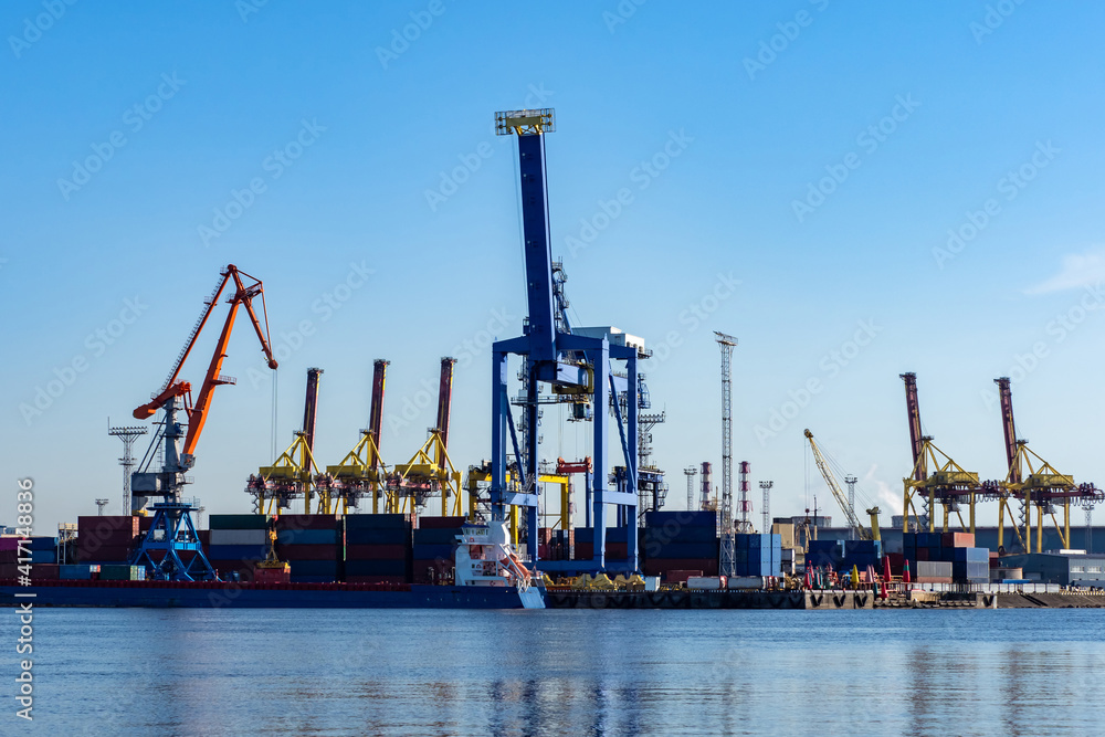 Crane at seaport. Cargo crane for loading containers. Loaders on sky background. Process of loading onto a cargo barge. Cargo transportation service concept by sea. Transportation on freight barge Crane at seaport. Cargo crane for loading containers. Loaders on sky background. Process of loading onto a cargo barge. Cargo transportation service concept by sea. Transportation on freight barge