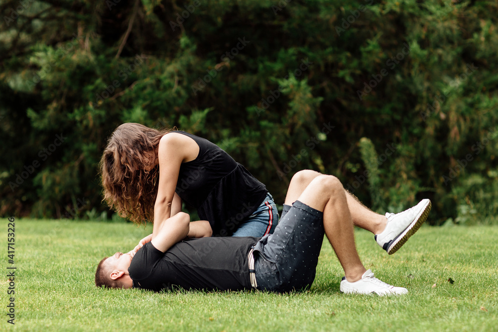 young couple is having fun and playing on the grass on summer day. woman lying over her lover, smiling