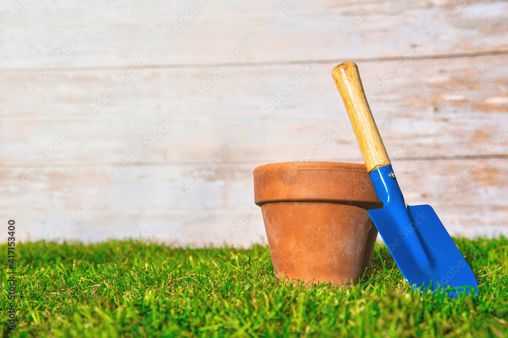 Flower pot empty with blue shovel in fresh green grass with wooden background texture, Garden,spring,hobby,potting concept copy space