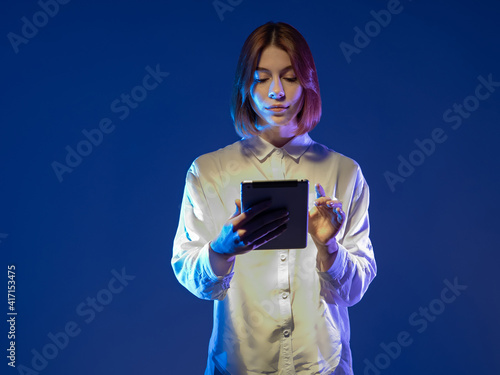 Young woman in trendy blouse holding tablet. Serious girl with tablet computer. Electronic tablet in hands of a man. She uses some kind of mobile app. Girl on a dark blue background. App for students photo