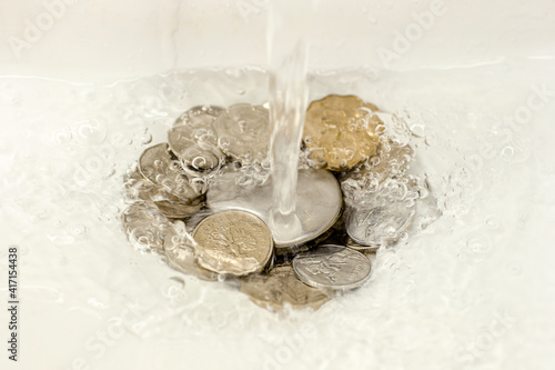 Faucet with water and coins. Money down the drain. Concept: expensive utilities. Water leakage, misuse of water. High cost of 