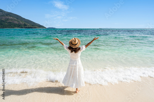 Young woman traveler relaxing and enjoying at beautiful tropical white sand beach with wave foam and transparent sea, Summer vacation and Travel concept