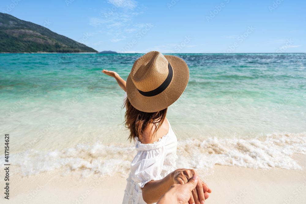 Young couple traveler holding hands relaxing and enjoying at beautiful tropical white sand beach with wave foam and transparent sea, Summer vacation and Travel concept