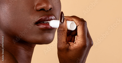 Black woman applying hygienic lip balm on light background