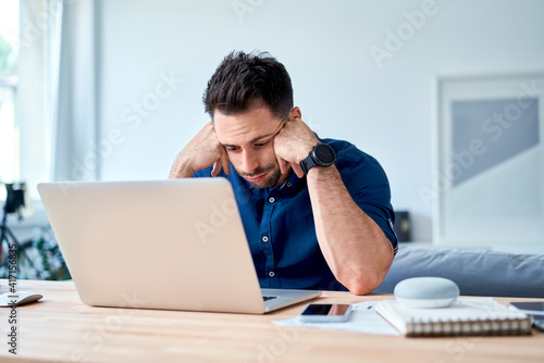 discouraged young man looking with disappointment on laptop while working at home photo