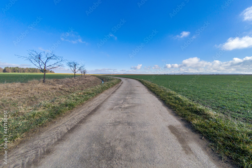 Dirty farm road with blue sky and green fields