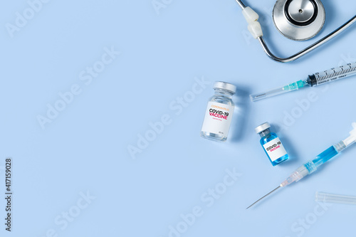 Fototapeta Naklejka Na Ścianę i Meble -  A vial of the Covid 19 vaccine with syringe and stethoscope on blue background,