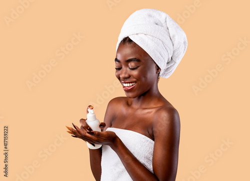 Smiling Black Woman In Towel Pouring Body Lotion On Palm