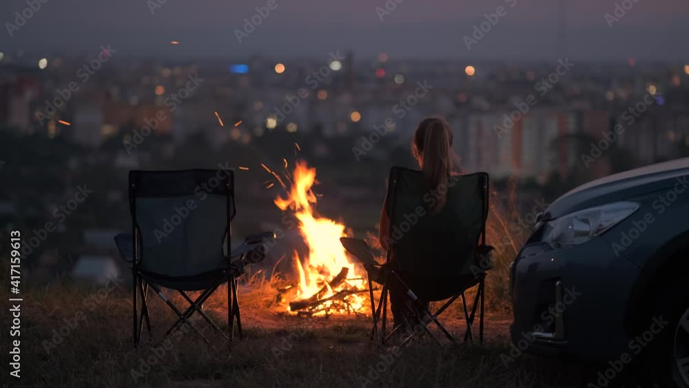 Dark silhouette of a lonely woman sitting on a chair near burning bonfire at night. Dark silhouette of a lonely woman sitting on a chair near burning bonfire at night.
