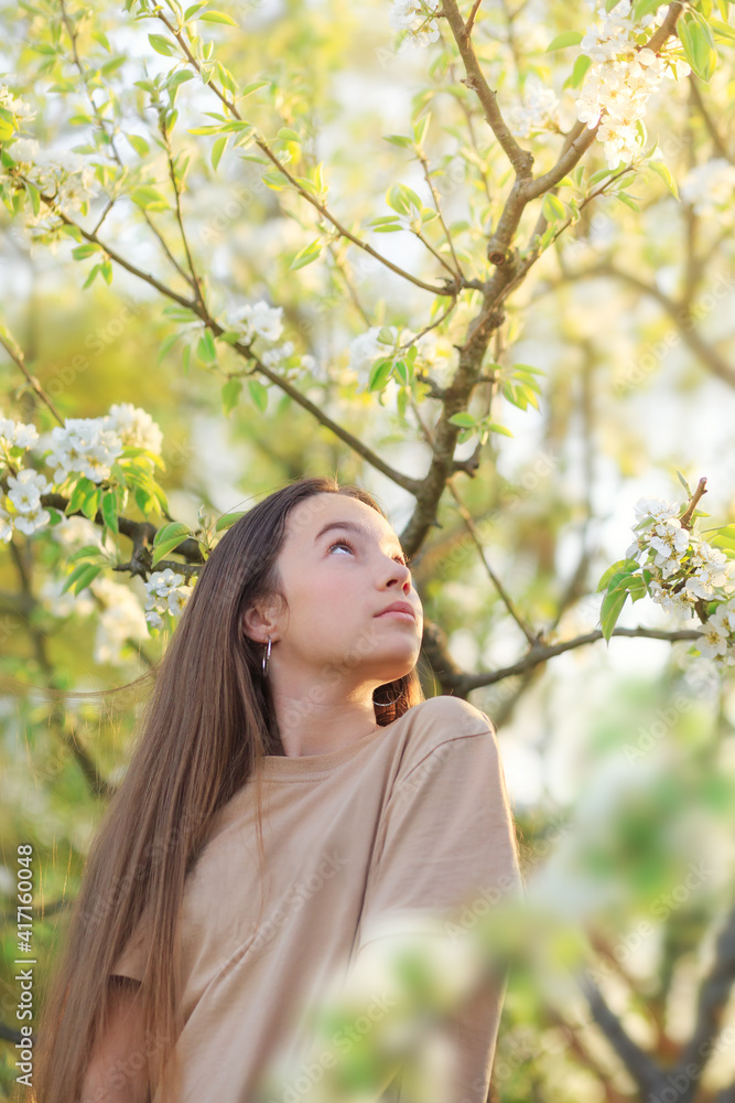 Beautiful teen girl with blooming apple flowers. Happy cute child having fun outdoors at sunset Beautiful teen girl with blooming apple flowers. Happy cute child having fun outdoors at sunset