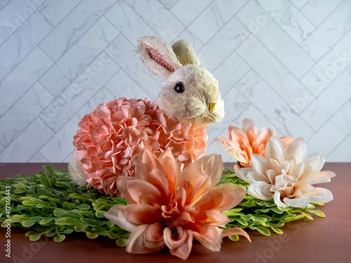 Easter Bunny Decor sitting on green leaves surrounded by peach artificial dahlia flower  blooms, perfect for the spring holiday! photo