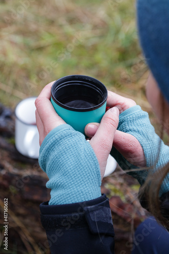 Woman drinking hot tea while hiking in the forest.